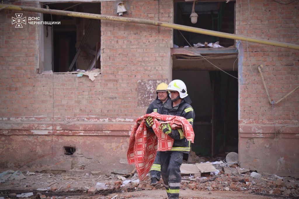 Two Ukrainian rescuers carry a bundle wrapped in a red plaid blanket away from a collapsed brick apartment building in Pryluky.